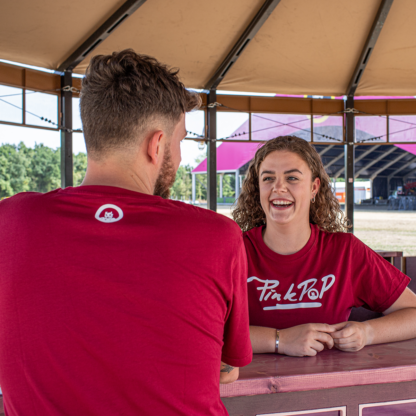 Man en vrouw met bordeaux rood shirt met witte Pinkpop-opdruk op borst en rond logo achter in nek van shirt gedrukt.