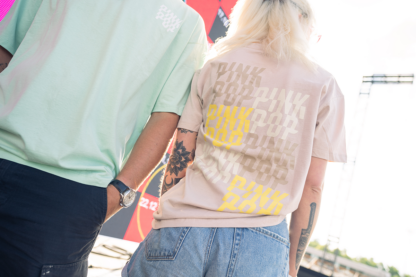 Vrouw met bruin shirt. Kleine Pinkpop-logo's op achterkant shirt in kleuren beige, bruin en geel.