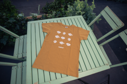 Foto van kids shirt okergeel met opdruk van signature pinkpop-oogjes en mondjes voor op borst