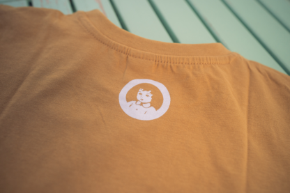 Foto van kids shirt okergeel met opdruk van rond pinkpop logo op achterkant.