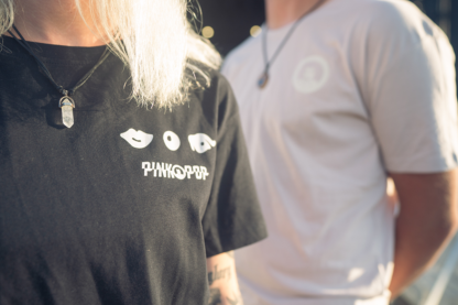 Vrouw met zwart shirt met signature Pinkpop-oogje, knoopje en mondje op linker borst gedrukt.