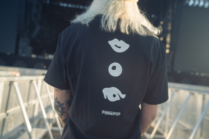 Vrouw met zwart shirt met signature Pinkpop-oogje, knoopje en mondje op rug gedrukt